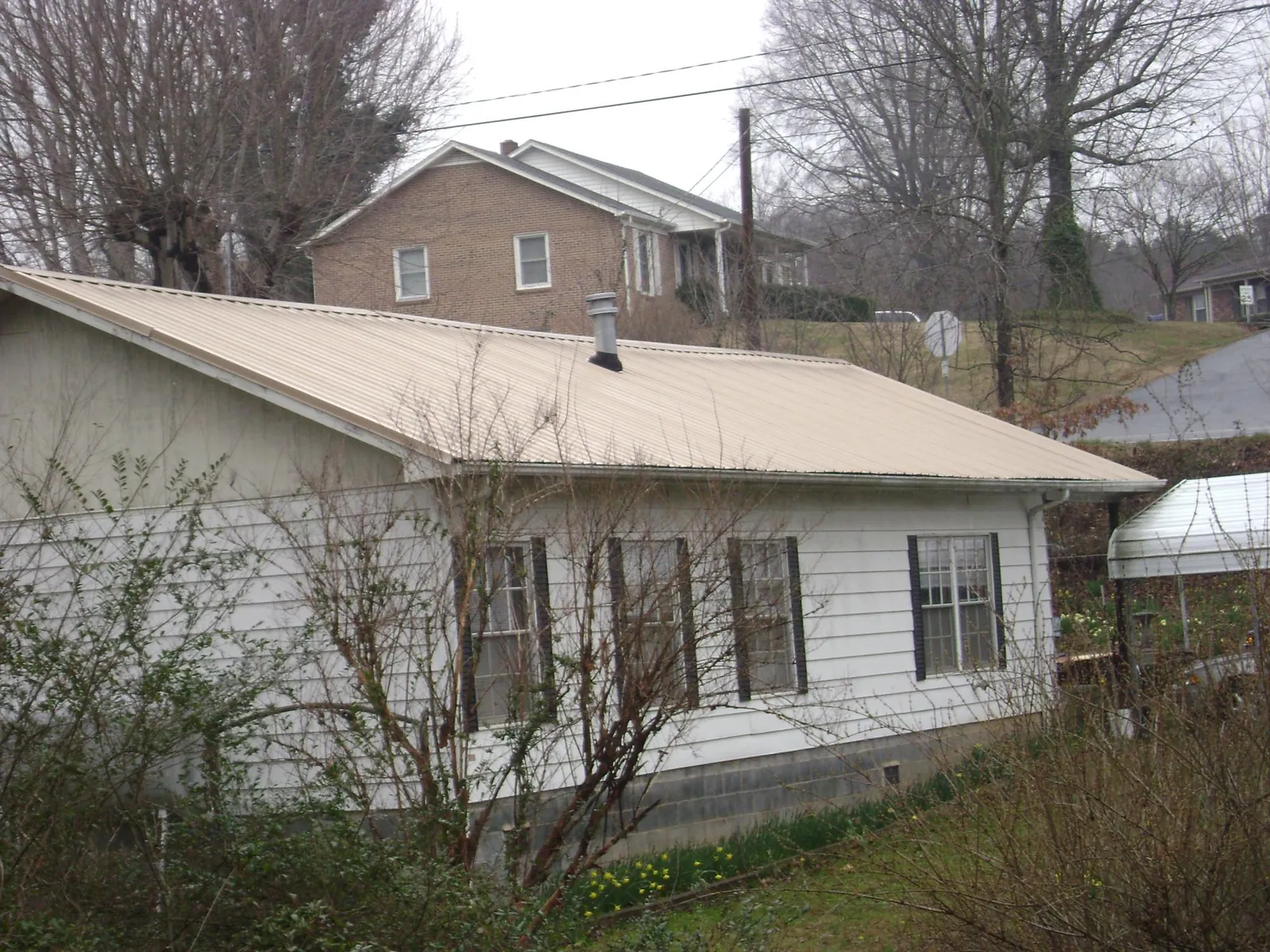 Tan metal roof on a white sided house set into a hillside — Commercial Roofing by Roofing Brothers in Hiram